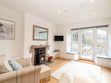 A living room with a fireplace armchairs a wall-mounted tv and large windows at Cliffside in Trebarwith Strand near Tintagel