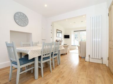 A dining area with a table and six chairs next to a living room with sofas and a wall-mounted TV at Cliffside in Trebarwith Strand near Tintagel