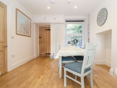 A dining room with wooden floor a table with chairs and a clock on the wall at Cliffside in Trebarwith Strand near Tintagel