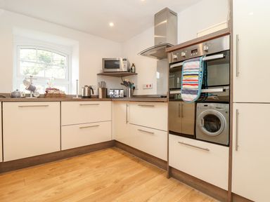 A kitchen with white cabinets wooden floor microwave kettle toaster and washing machine at Cliffside in Trebarwith Strand near Tintagel