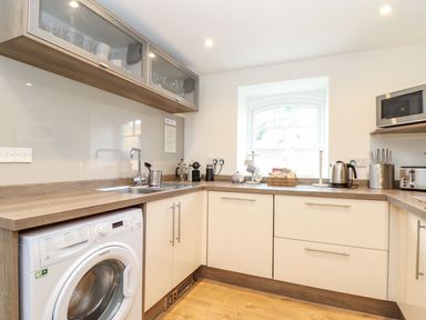A kitchen with a washing machine sink microwave kettle and cabinets at Cliffside in Trebarwith Strand near Tintagel