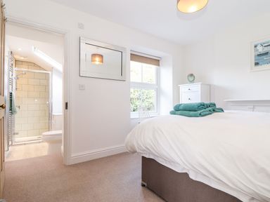 A bedroom with a bed with folded towels on it a window a white dresser and an open door leading to a bathroom with a shower at Cliffside in Trebarwith Strand near Tintagel