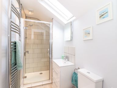 A bathroom with a glass shower enclosure a white sink and vanity a toilet and decorative pictures on the wall at Cliffside in Trebarwith Strand near Tintagel
