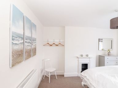 A bedroom with a bed dresser mirror chair coat hooks and fireplace at Cliffside in Trebarwith Strand near Tintagel
