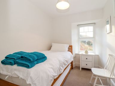 A small bedroom with a single bed towels on the bed a bedside table with a lamp and a chair by the window at Cliffside Trebarwith Strand near Tintagel