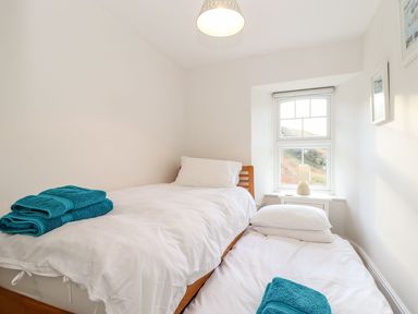 A bedroom with two single beds white bedding blue towels and a window at Cliffside in Trebarwith Strand near Tintagel