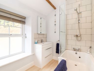 A bathroom with a bathtub shower combination a sink cabinet window and a mirror at Cliffside Trebarwith Strand near Tintagel