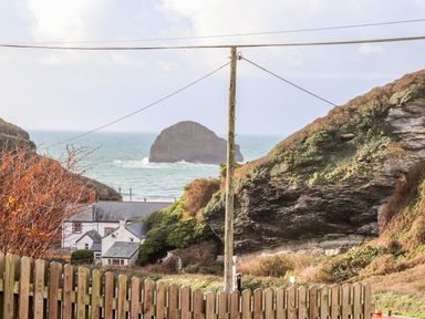 A view of rocky cliffs sea and houses behind a wooden fence at Cliffside in Trebarwith Strand near Tintagel