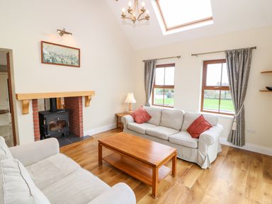 A living room with two sofas a wooden coffee table a wood stove and two windows at Ballycahane Castletownshend County Cork
