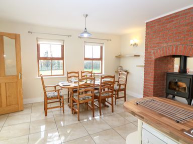 A dining area with a wooden table and six chairs near two windows and a brick fireplace at Ballycahane in Castletownshend County Cork