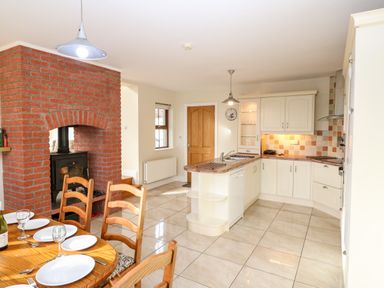 A kitchen with white cabinets a tiled floor a wooden dining table with chairs and a brick fireplace at Ballycahane in Castletownshend County Cork