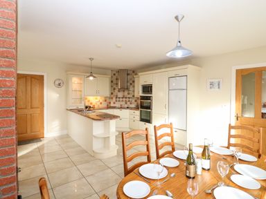 A kitchen and dining area with wooden chairs a table set with plates glasses and bottles at Ballycahane in Castletownshend County Cork