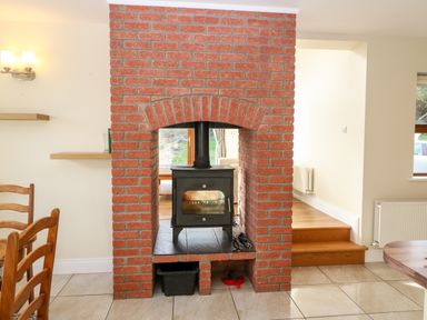 A brick fireplace with a black wood stove inside and wooden chairs nearby at Ballycahane in Castletownshend County Cork
