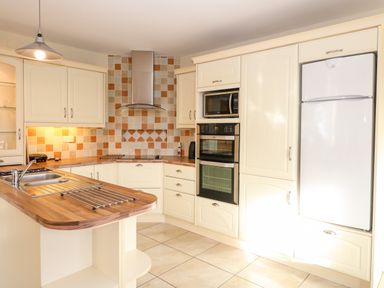 A kitchen with cream cabinets a wooden countertop tiled backsplash a double oven a microwave and a white refrigerator at Ballycahane in Castletownshend County Cork