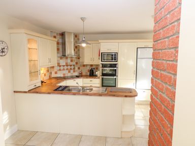 A kitchen with white cabinets wooden countertops a double sink a wall clock a built-in oven microwave and a refrigerator at Ballycahane in Castletownshend County Cork