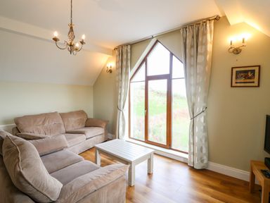 A living room with two beige sofas a white coffee table and a large window with curtains at Ballycahane in Castletownshend County Cork
