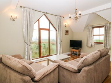 A living room with two sofas a coffee table a TV on a stand and large windows at Ballycahane in Castletownshend County Cork