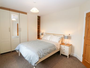 A bedroom with a bed a bedside table with lamps a wardrobe with a mirror and a wooden door at Ballycahane in Castletownshend County Cork