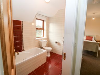 A bathroom with a bathtub toilet and tiled floor next to a bedroom with a bed and pillow at Ballycahane in Castletownshend County Cork