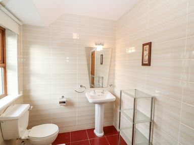 A bathroom with a toilet a pedestal sink a mirror a glass shelving unit and a window at Ballycahane in Castletownshend County Cork