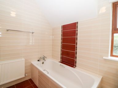 A bathroom with a bathtub a towel rack a radiator and a window at Ballycahane in Castletownshend County Cork