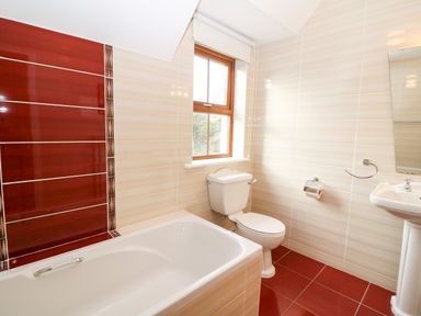 A bathroom with a bathtub toilet sink and window with red and beige tiles at Ballycahane in Castletownshend County Cork
