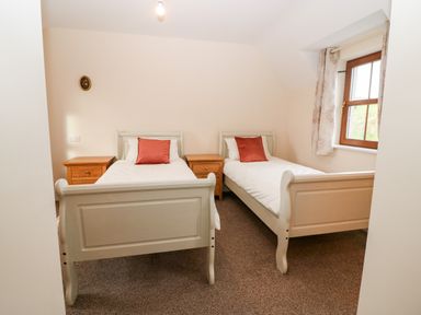 A bedroom with two single beds with white bedding and red pillows two wooden nightstands and a window with floral curtains at Ballycahane in Castletownshend County Cork