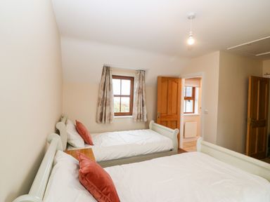 A bedroom with two single beds white bedding red pillows a wooden window with curtains and wooden doors at Ballycahane in Castletownshend County Cork