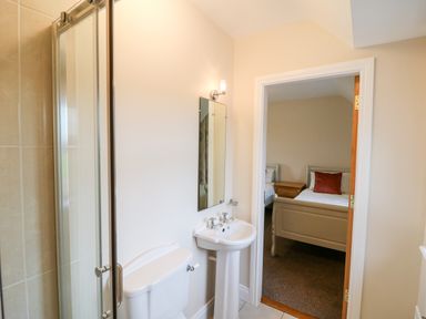 A bathroom with a shower, toilet, sink, mirror, and a doorway leading to a bedroom at Ballycahane in Castletownshend County Cork