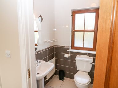 A bathroom with a white sink toilet a brown window and a waste bin at Ballycahane Castletownshend County Cork