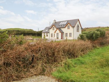 A house with multiple windows and solar panels on the roof surrounded by bushes and grass at Ballycahane in Castletownshend County Cork
