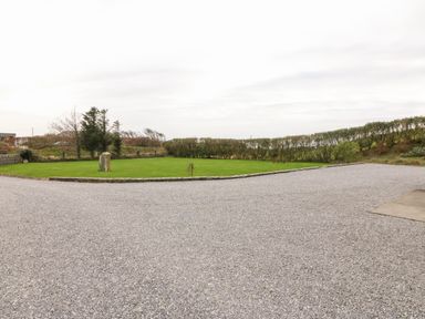 A gravel driveway with a grass lawn and stone edging surrounded by trees and shrubs at Ballycahane in Castletownshend County Cork