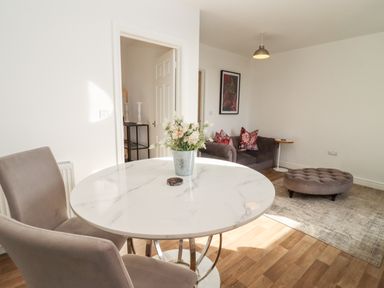 A room with a round white marble table and two chairs a grey sofa with cushions and a grey ottoman on a rug at Stillness in Blandford Forum