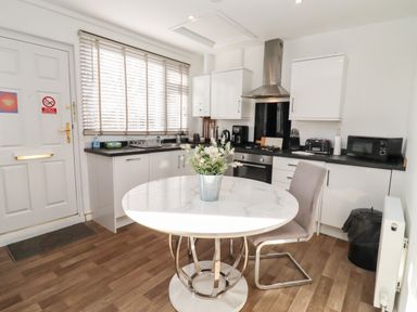 A kitchen with a round table and a chair in front of cabinets and appliances at Stillness in Blandford Forum