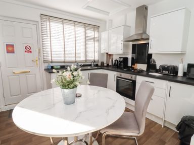 A kitchen with a round table and chairs a stove a toaster and a window with blinds at Stillness in Blandford Forum