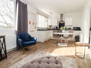 A kitchen and dining area with a round table and two chairs a blue armchair and a cushioned ottoman at Stillness in Blandford Forum