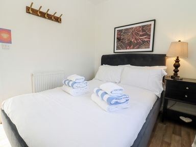 A bedroom with a made bed that has folded towels on it a nightstand with a lamp and a framed picture on the wall at Stillness in Blandford Forum