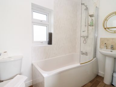 A bathroom with a bathtub shower combination toilet sink and a round mirror at Stillness in Blandford Forum