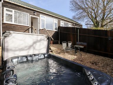A backyard with a hot tub a small table and two chairs outside a wooden house at Stillness in Blandford Forum