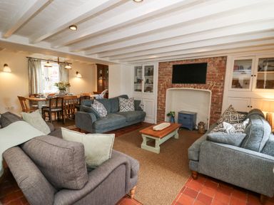 A living room with three sofas a coffee table a wall-mounted television and a dining table with chairs at Dyffryn Cottage in Aberporth