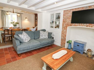 A living room with a sofa coffee table wood stove and dining table with chairs at Dyffryn Cottage in Aberporth