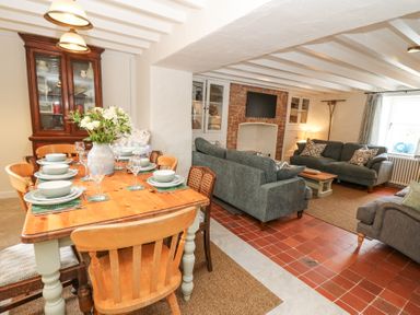 A dining table set with dishes and glasses next to a living area with sofas and a television at Dyffryn Cottage in Aberporth