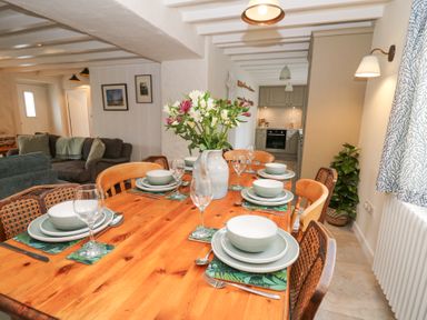 A dining table with plates glasses and a vase of flowers in a room with a sofa and kitchen in the background at Dyffryn Cottage in Aberporth