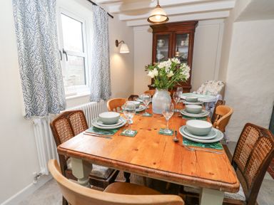 A dining room with a wooden table set with plates bowls glasses and flowers at Dyffryn Cottage in Aberporth