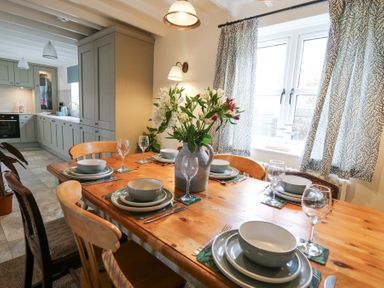 A dining table set with plates bowls and wine glasses near a window in a kitchen at Dyffryn Cottage in Aberporth