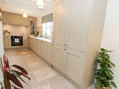 A kitchen with beige cabinets a sink oven two pendant lights and plants at Dyffryn Cottage in Aberporth
