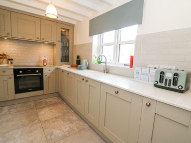 A kitchen with beige cabinets a built-in oven a sink under a window and small kitchen appliances at Dyffryn Cottage in Aberporth