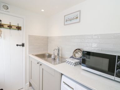 A kitchen sink with soap dispenser a microwave and a washing machine under the counter at Dyffryn Cottage in Aberporth