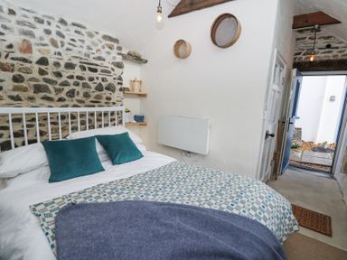 A bedroom with a bed with teal pillows stone wall wooden shelves and an open door at Dyffryn Cottage in Aberporth