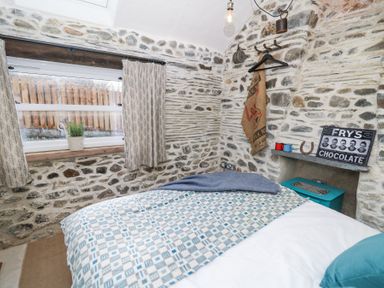 A bedroom with a bed a window with curtains and stone walls at Dyffryn Cottage in Aberporth